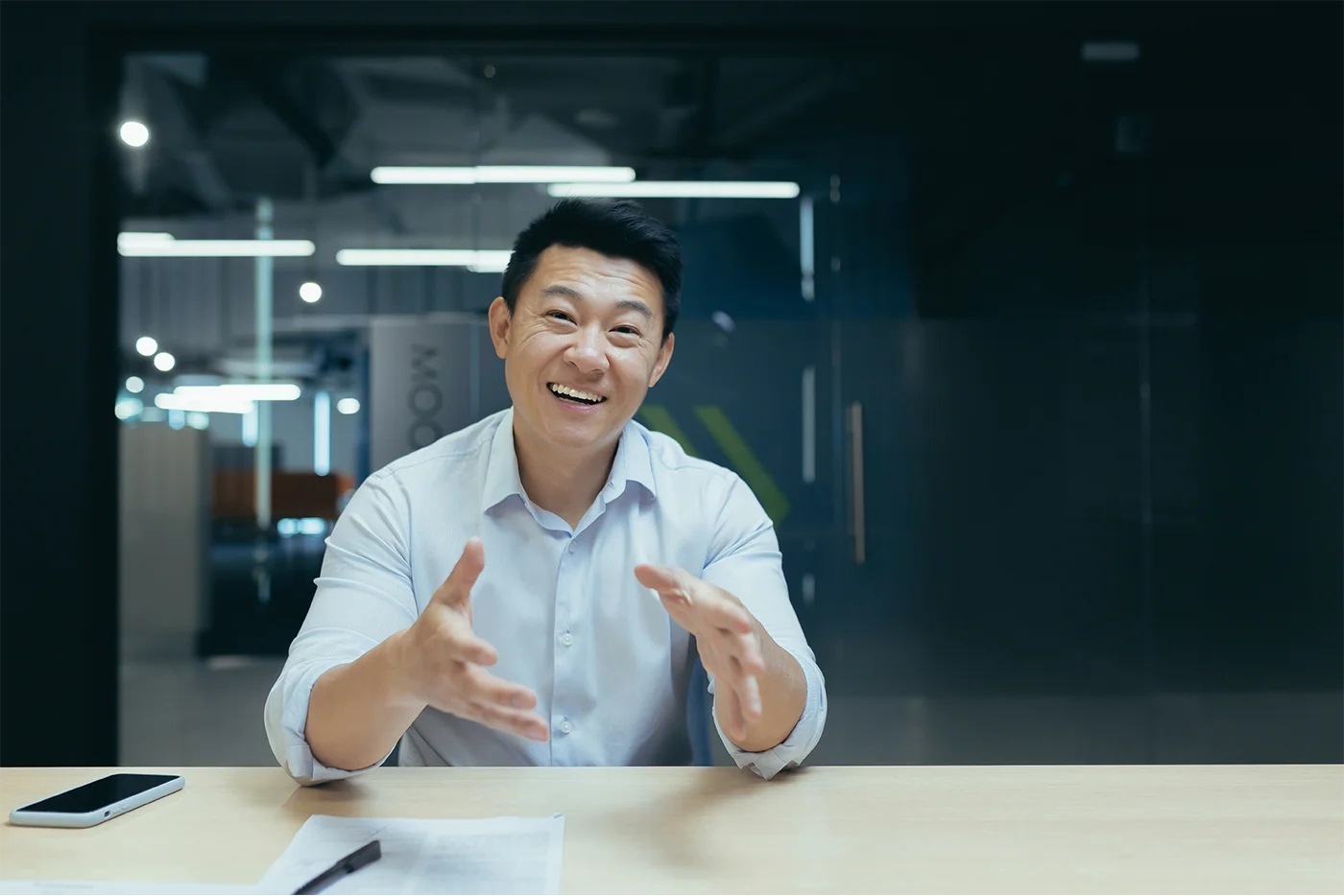 A corporate man presents across a wooden table, he is smiling and talking animatedly with his hands.